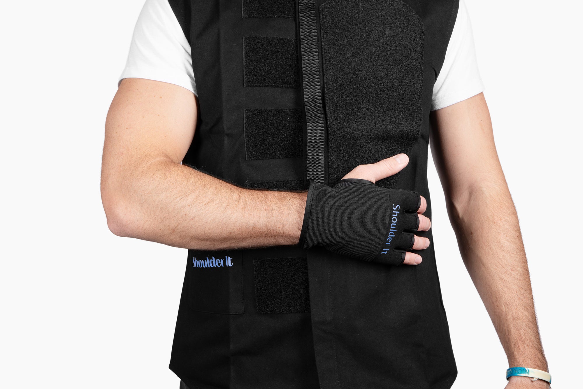 Close-up side view of a man wearing the Shoulder It vest, showing his arm bent and hand resting comfortably across his body using the built-in glove and strap. The product helps shoulder surgery patients sleep better by reducing pressure points from traditional slings.
