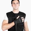 A man recovering from shoulder surgery wears a black Shoulder It recovery vest over a white t-shirt, with his right hand positioned across his chest and secured by a glove and strap system. This front-facing image highlights how the vest supports comfortable hand positioning during recovery. Shoulder It is an alternative to traditional shoulder slings, designed to improve sleep after rotator cuff surgery, labrum repair, or shoulder replacement.